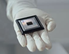 a white gloved hand holding a square silver chip with another black square in the middle